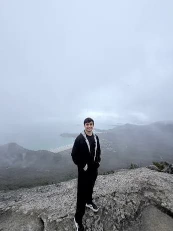 Manav standing on a rocky summit above the clouds